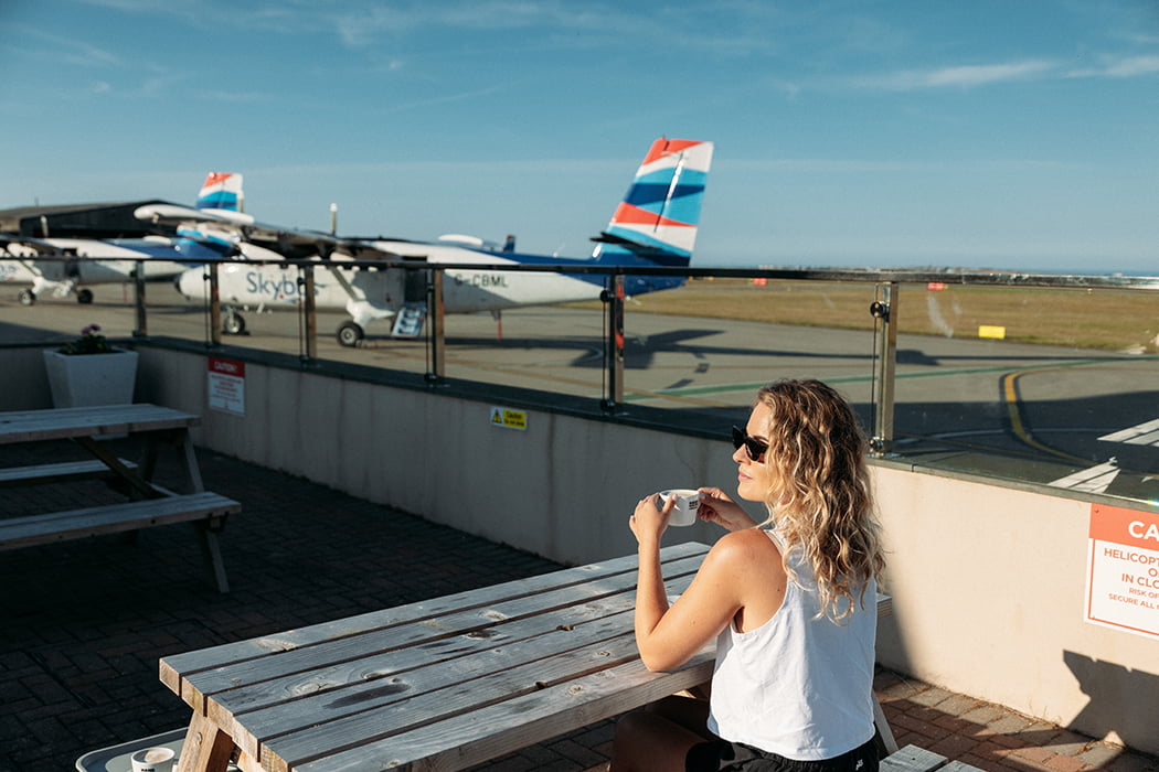 woman having coffee outside on the cafe terrace with views on to the airfield - Land's End Airport, Cornwall 