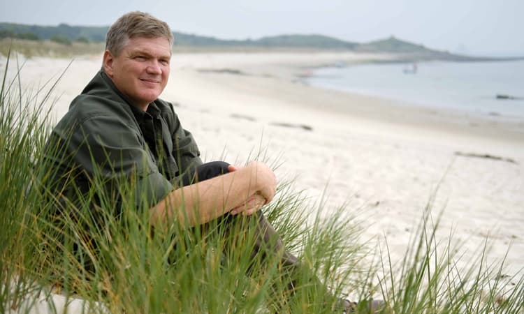Ray Mears sitting on a beach on St Martin's, Isles of Scilly in June