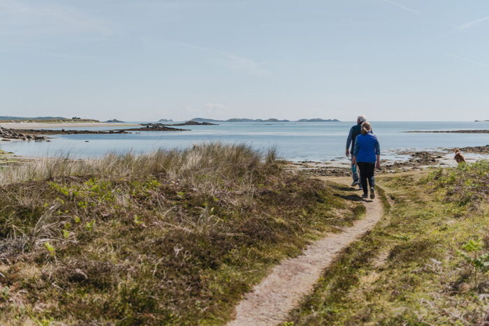 Older couple walking the coastal path with their dog, Pentle Bay, Tresco
