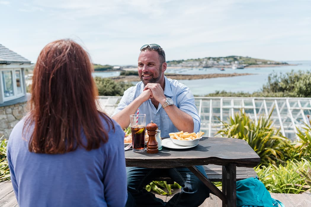 Couple enjoying alfresco dining in a restaurant with harbour views on St Mary's, Isles of Scilly