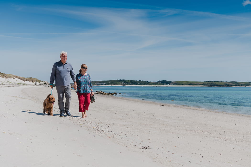 Couple walking their dog on a lead on a beach, Tresco, Isles of Scilly