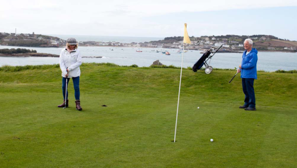 Isles of Scilly Gold course - A couple playing golf with a view of St Mary's