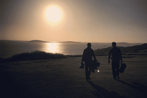 Isles of Scilly Golf course at sunset with two players finishing a round of golf
