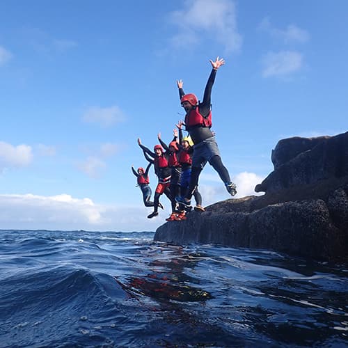 a group of people on a coasteering tour star jumping from Peninnis head, St Marys