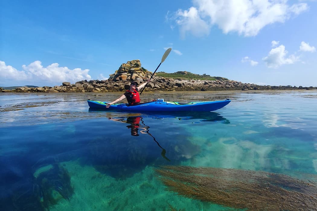 person in a blue kayak on a tour around the Isles of Scilly on a sunny day