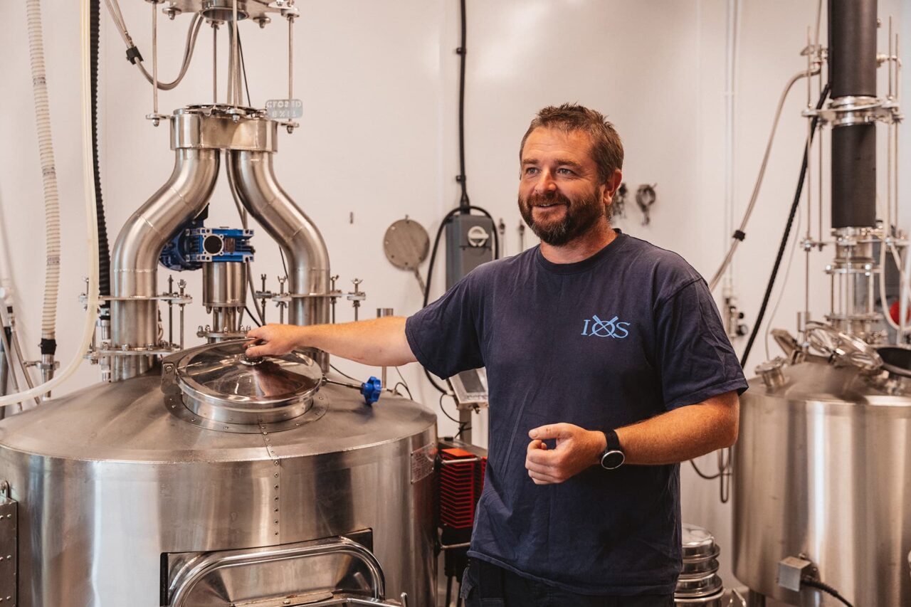 Andrew the owner of SC Dogs standing next to distillery equipment