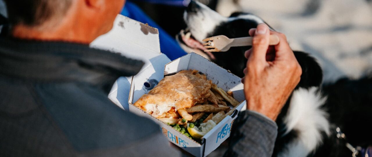 man eating fish and chips with his dog