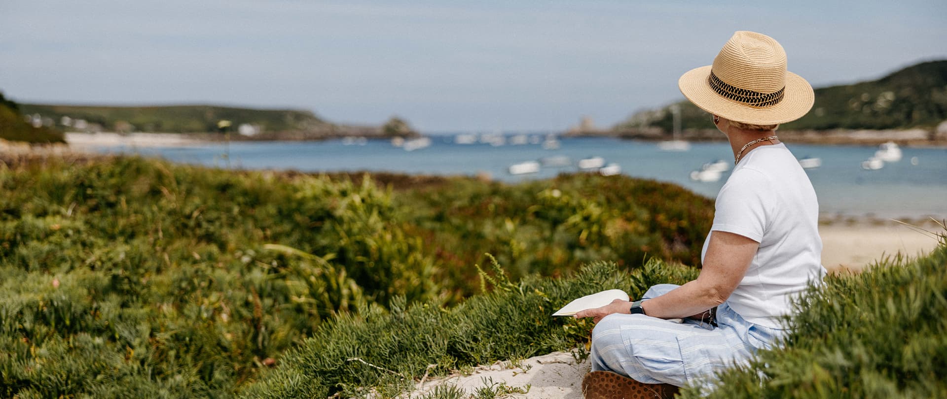 Woman sitting down drawing the view of the channel between Tresco and Bryher, Isles of Scilly