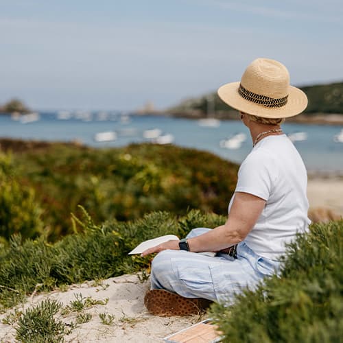 Woman sitting down drawing the view of the channel between Tresco and Bryher, Isles of Scilly