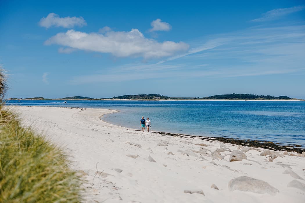 Couple walking along Bar Point beach, St Mary's Isles of Scilly on a sunny summer's day