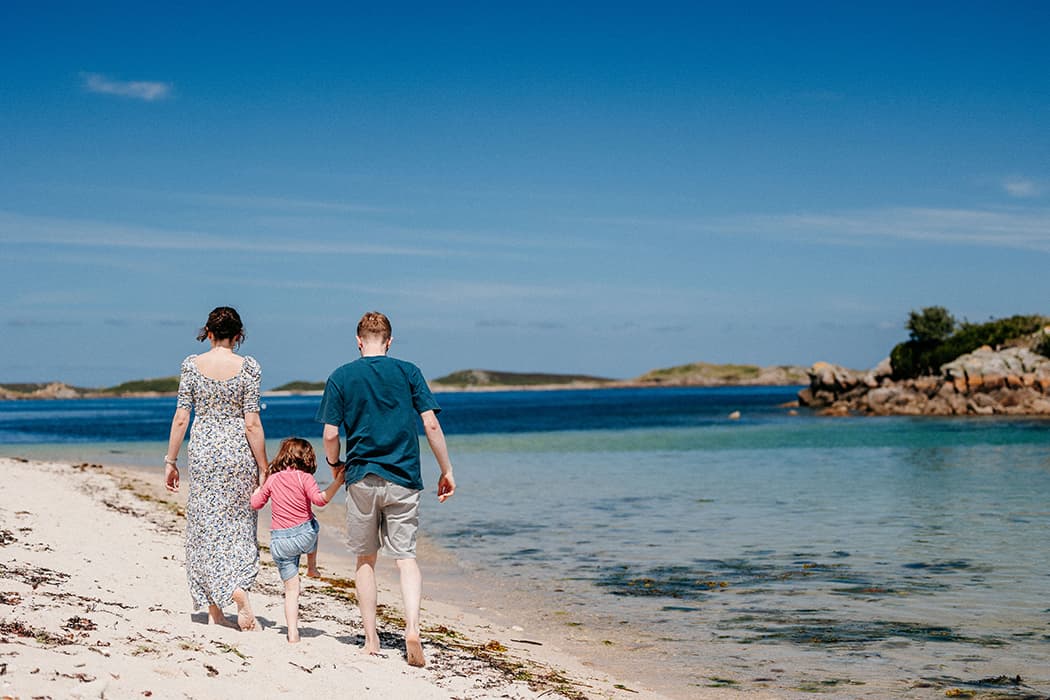 Family of three walking along Bar Point beach, St Mary's Isles of Scilly on a sunny summer's day