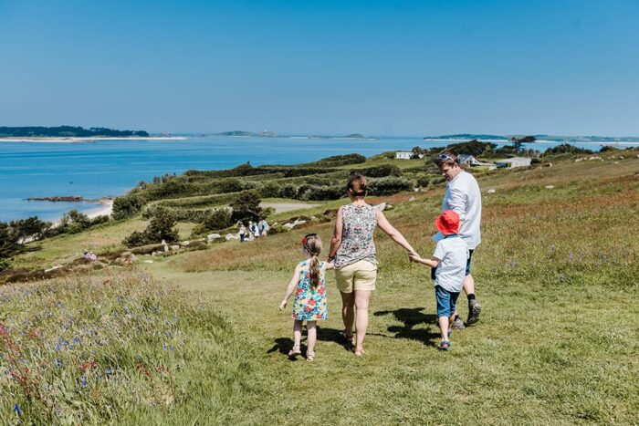 Family walking St Mary's coastal path with views looking towards Tresco, Isles of Scilly