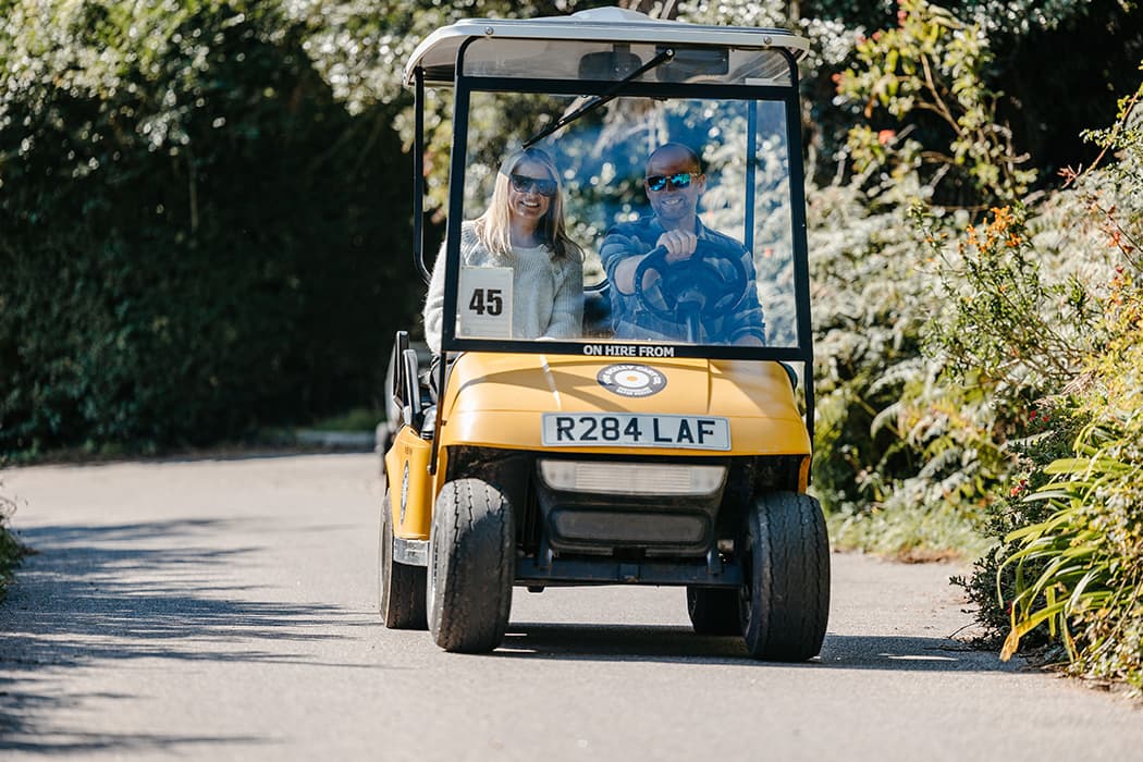 A couple driving a yellow scilly golf cart on St Mary's