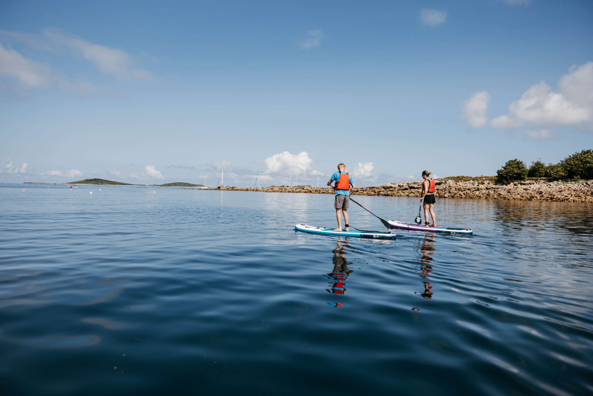 Two people stand up paddle boarding on a beach in St Mary's 